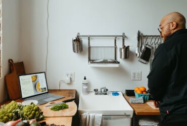 a man standing in a kitchen next to a laptop computer