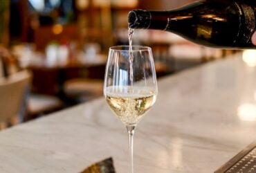 person pouring liquid in clear wine glass