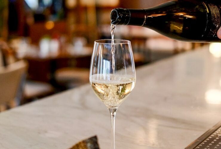 person pouring liquid in clear wine glass
