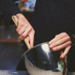 a person stirring a pot with a wooden spoon